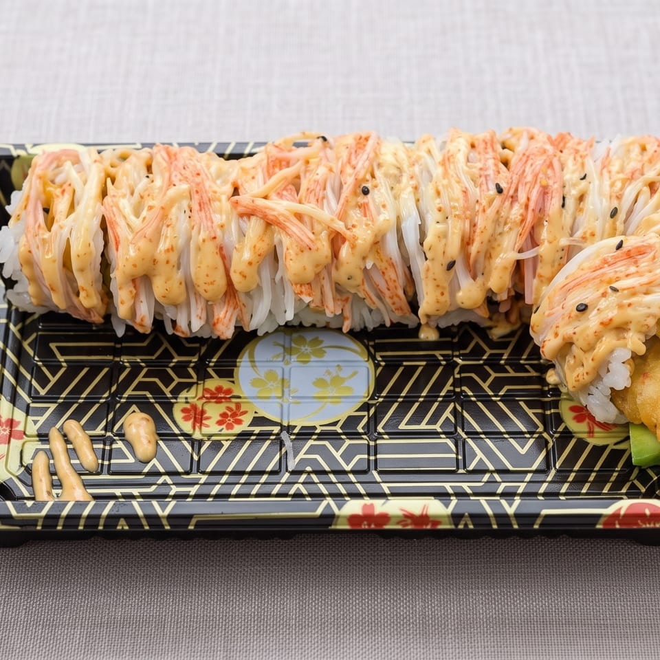 Sushi roll topped with shredded imitation crab and creamy orange sauce on a decorative black platter.